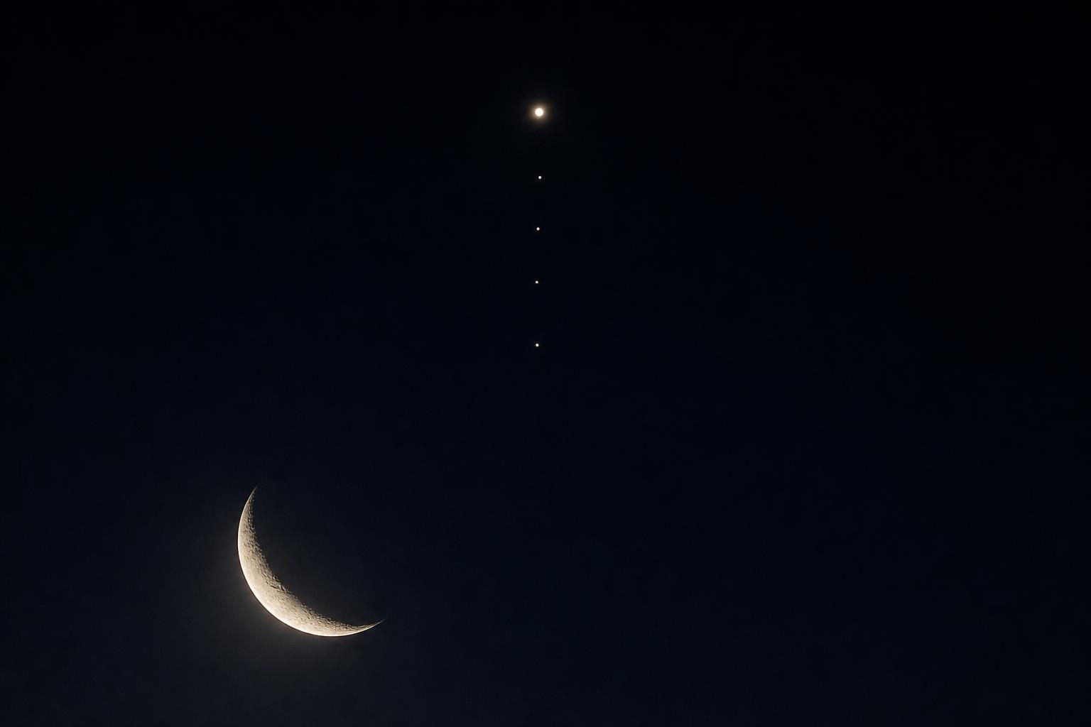 A crescent Moon appears below Jupiter and four small moons lined up in the night sky.